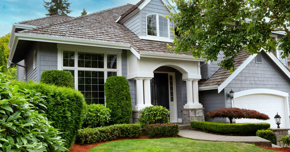 A house with a large front yard. The house has gray-and-white tones that blend well with the roofing color.