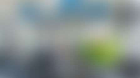 A person wearing a white hard hat and a bright yellow high-visibility jacket is inspecting a large industrial pump.