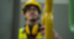 A worker in a yellow hard hat and safety vest inspects a bright yellow industrial pipe in an indoor facility.