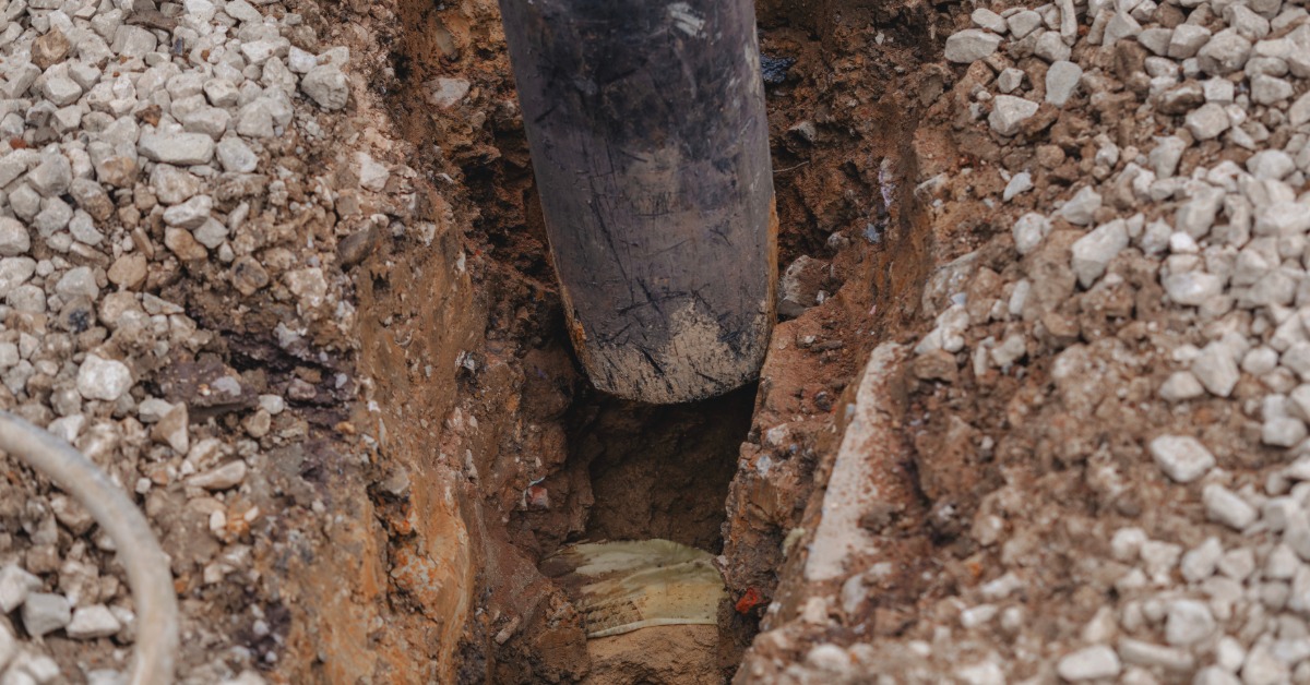 A hole is dug into the ground, and a black tube is placed inside of the hole. Rocks surround the top of the hole.