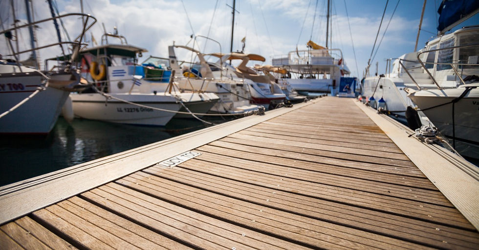 A wooden marina dock extends between moored boats, with white hulls, ropes, and masts lining both sides.