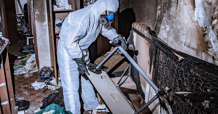 Image 3: A person with a respirator and is lifting up a fire damaged object. The room they are in has signs of fire damage all around.