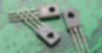 Three tiny transistors used in modern electronics sit on top of a green and silver hard-drive panel.