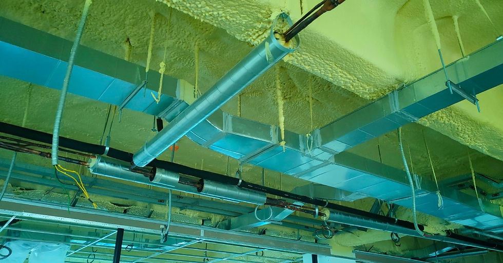 The ceiling of an industrial building with spray foam insulation all over it. The airducts are covered with protective tape.