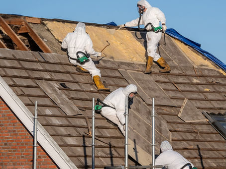 Several people are on a roof of a house. They are all wearing protective gear as they tear the roof apart.