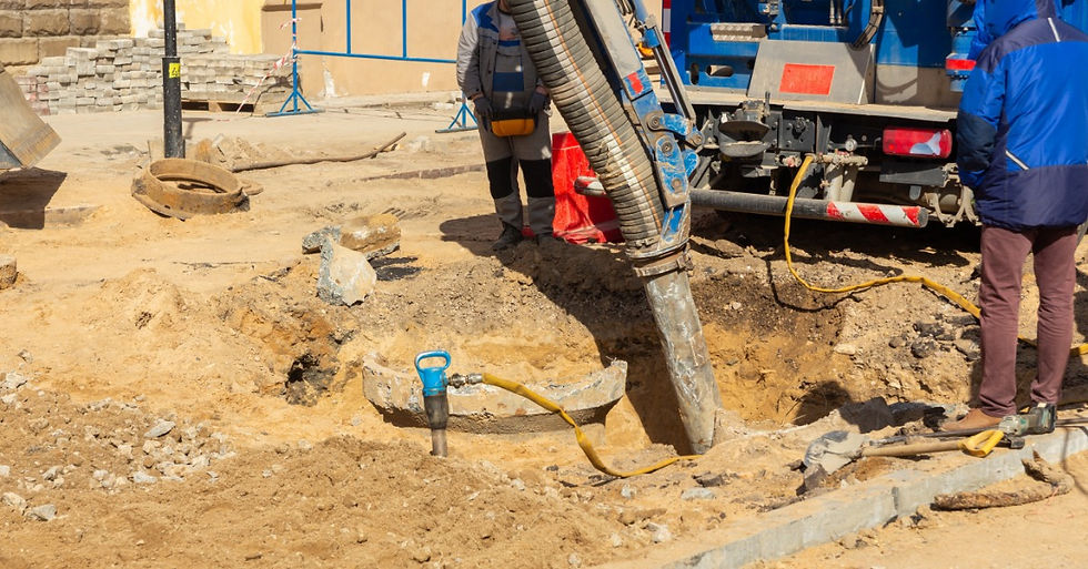 Two people are standing next to a hole in the ground. There is a black hose running down the hole.