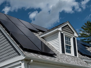 The roof of a house with solar panels. The house has white trim along the windows and white siding on the lower floor.