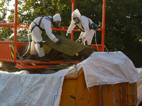 Two people are on an orange platform as they toss garbage into a dumpster. They’re both wearing protective equipment.