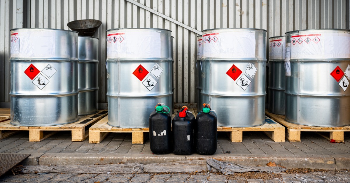 Silver barrels are stacked up on individual pallets. The barrels all have warning labels on them.