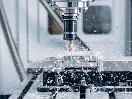 Close-up of CNC milling machine cutting metal block, coolant spraying as rotating drill shapes precision part.