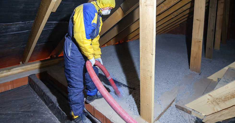 A man is in an attic; he’s wearing protective gear as he’s holding a red spray hose. There is insulation on the ground.