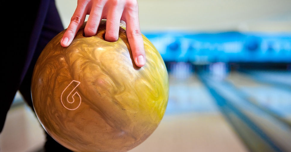 A person stepping up to a bowling lane, preparing to throw a mustard yellow ball with a subtle swirl pattern.