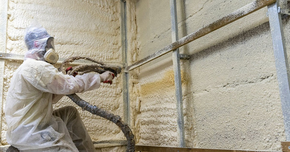 A person wearing a full body protective suit and mask holding a hose while spraying foam into the wall of a building.