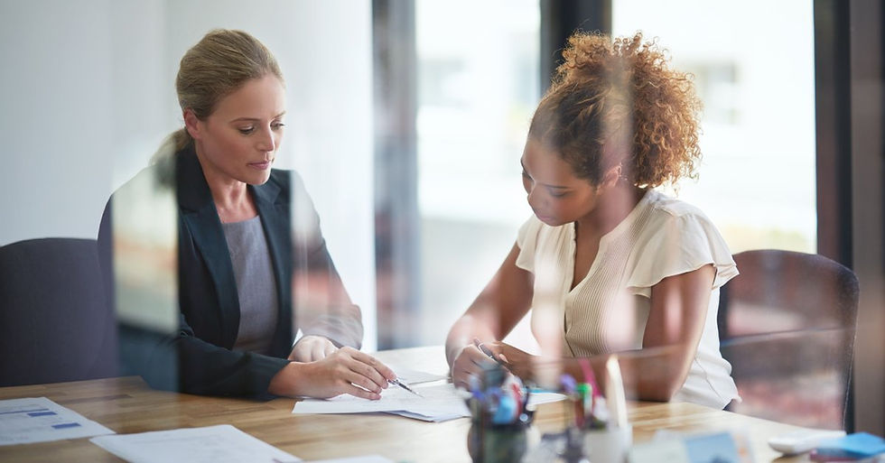 Two women sitting across a table from one another in an office with a glass door while going over financial documents.