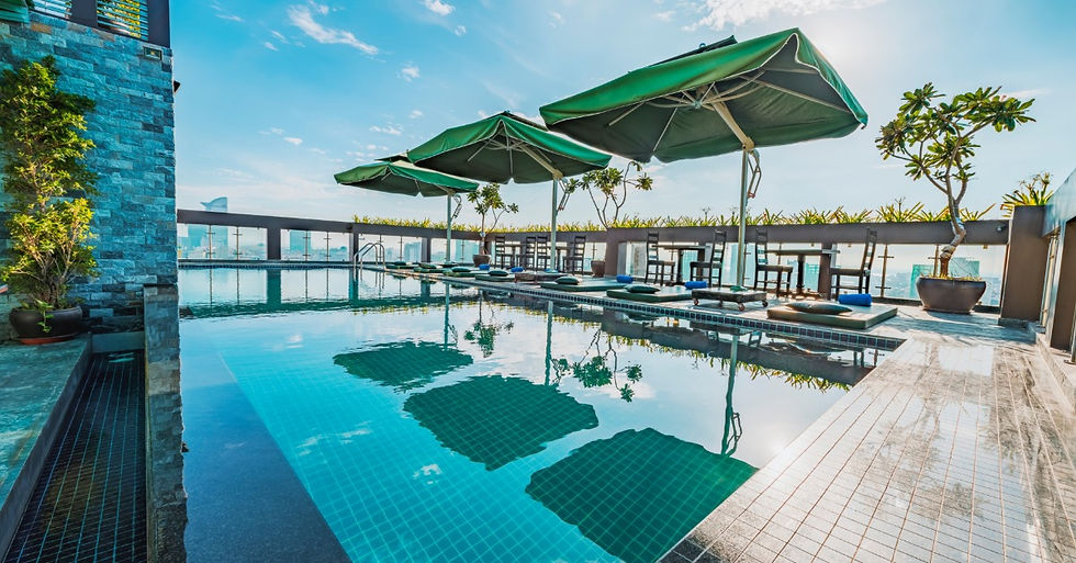 A hotel's rooftop swimming pool features bright blue water. Deck chairs and plants sit on the side of the pool.