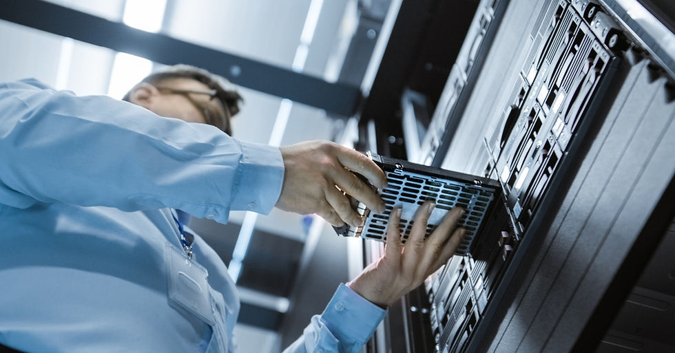 An IT engineer installs a hard drive into a server rack in a fully operational data center from a low angle.