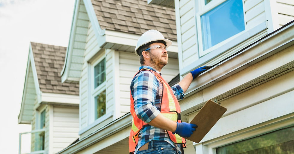 A man wearing a white hard hat, safety vest, and blue gloves inspecting a house roof while holding a clipboard.