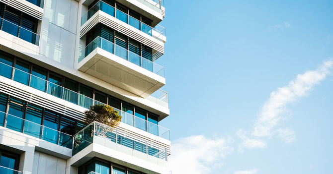 The corner of a building, featuring many balconies and several blue windows. A clear blue sky is in the background.