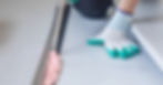 A technician kneeling down wearing gloves holding a can of spray foam while applying it into a crack in the floor.