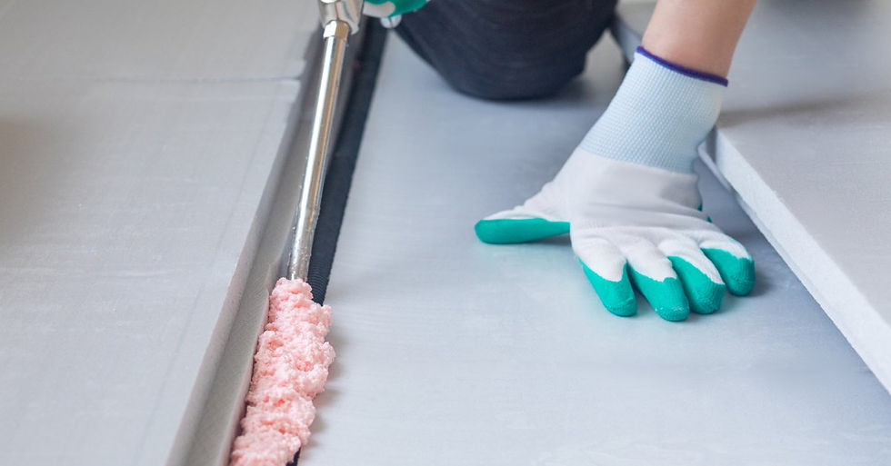 A technician kneeling down wearing gloves holding a can of spray foam while applying it into a crack in the floor.