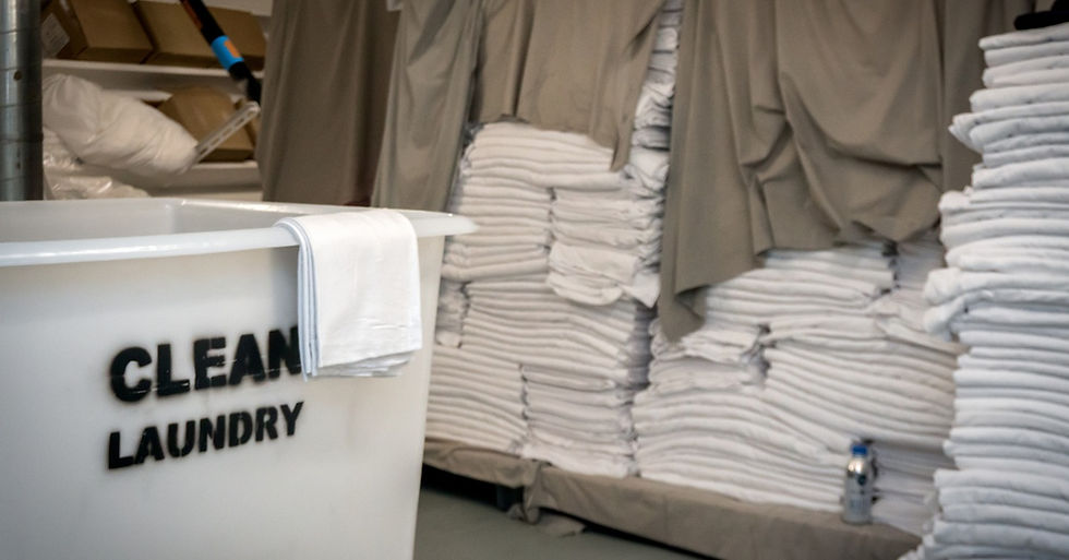 Multiple stacks of towels and linens in a storage space next to a white plastic bin labeled with the words "clean laundry."