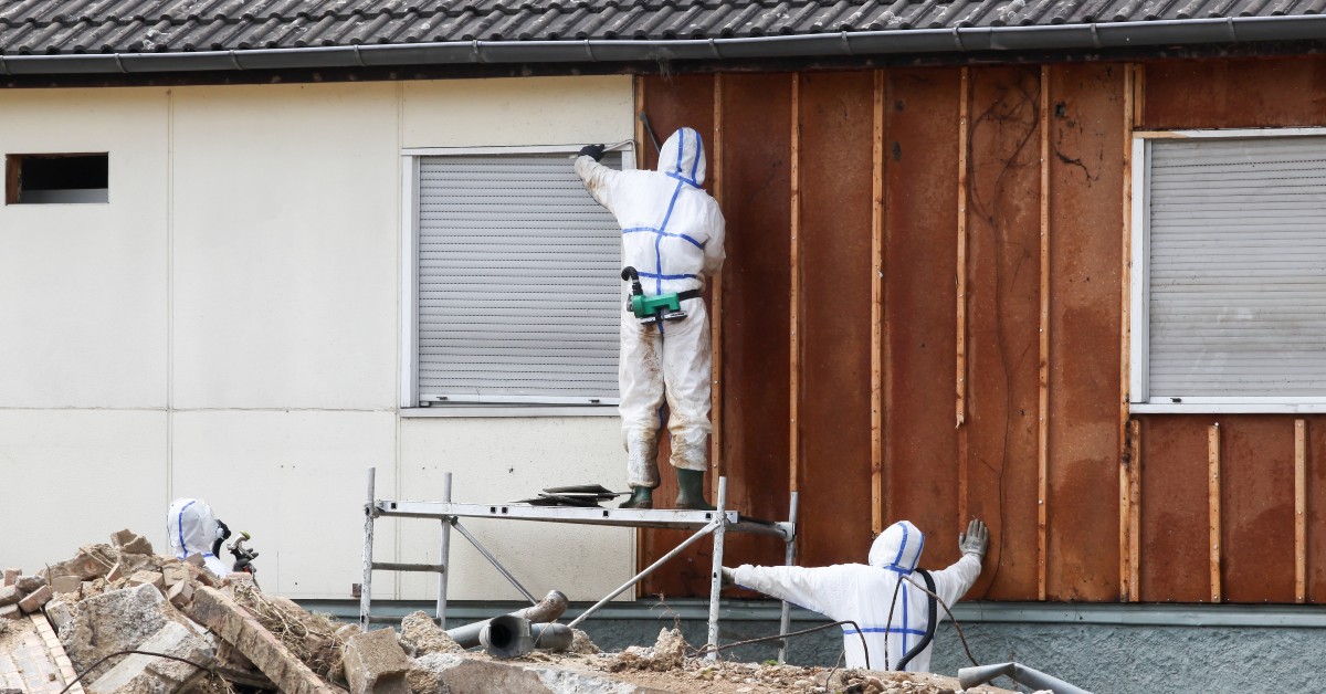 Two people are working on the side of a building. They are both wearing protective clothing.
