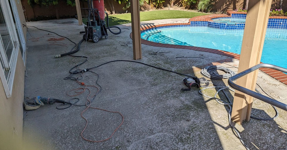 A covered poolside patio with concrete flooring, hoses, cords, tools, and equipment beside blue water.