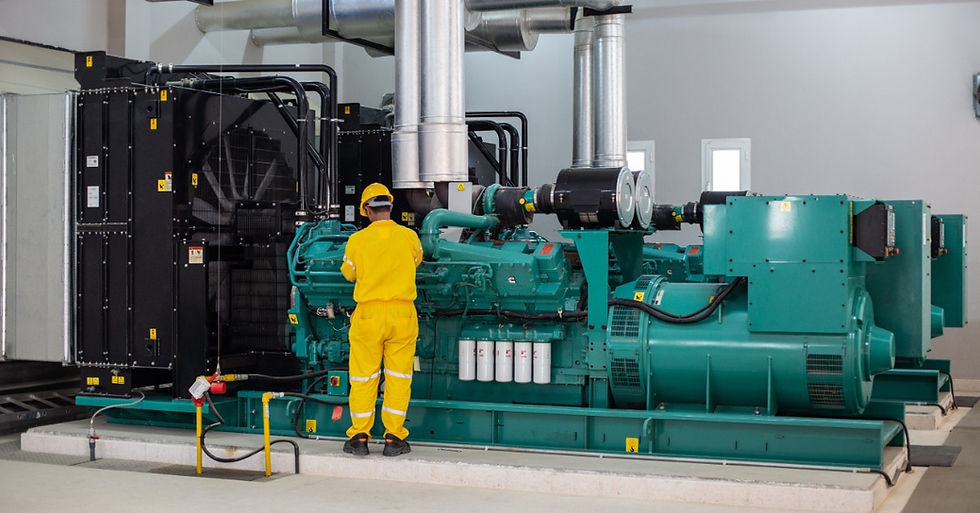 A man wearing a yellow work suit and a yellow hard hat is looking at a large, teal industrial generator.