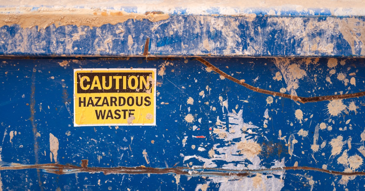 A yellow and black sticker that warns of hazardous material is stuck to a metal surface that is painted blue.