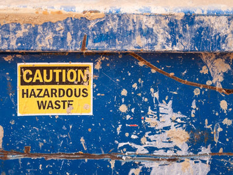 A yellow and black sticker that warns of hazardous material is stuck to a metal surface that is painted blue.