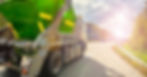 A truck with a green trailer on its bed is driving down a road. The sun is shining and there’s another car on the road.