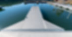 A silver aluminum dock with no boats around it extends into a still lake surrounded by forests and mountains.
