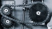 Two dark-colored chains are wrapped around different gears inside a machine. The gears are dark-colored, too.