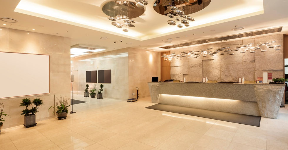 A hotel lobby features a stone desk and a white marble wall behind it. It has lighting with mirrors in its ceiling.