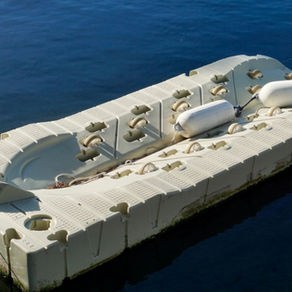 Floating modular dock platform anchored on calm water, made of interlocking plastic blocks with mooring lines.