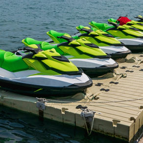 A row of bright green jet skis is lined up on a floating dock, secured with ropes on calm open water.