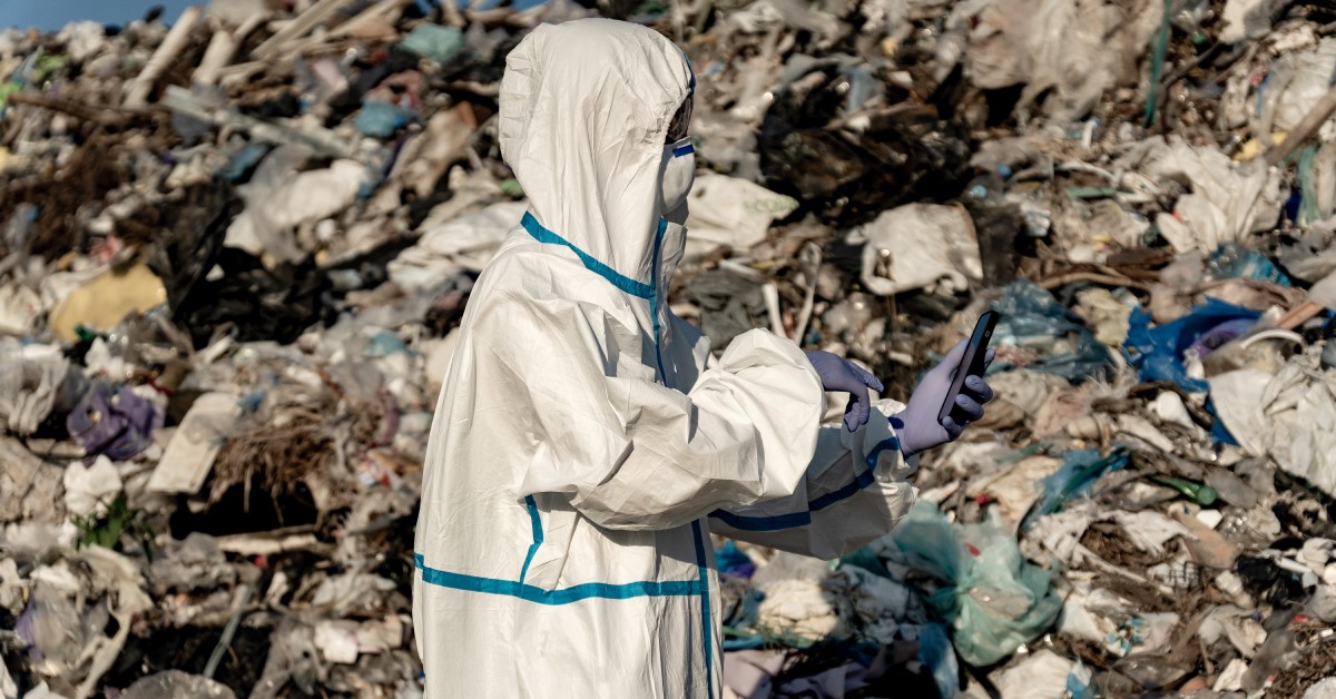 A person is wearing a white jumpsuit. Behind them is a hill made of garbage and other refuse.