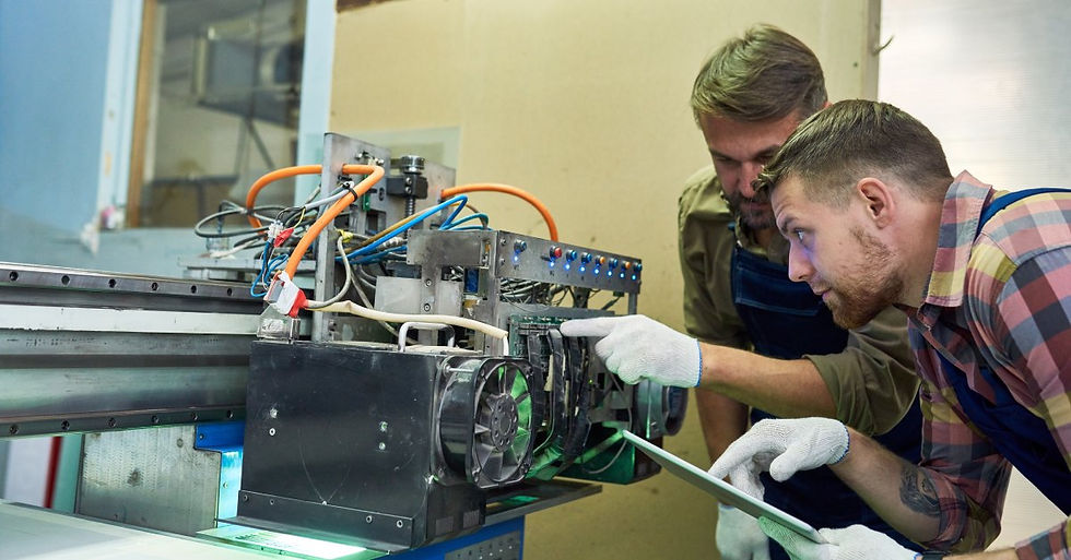 Two men wearing white gloves lean down in front of the exhaust fans of a machine, inspecting its parts.
