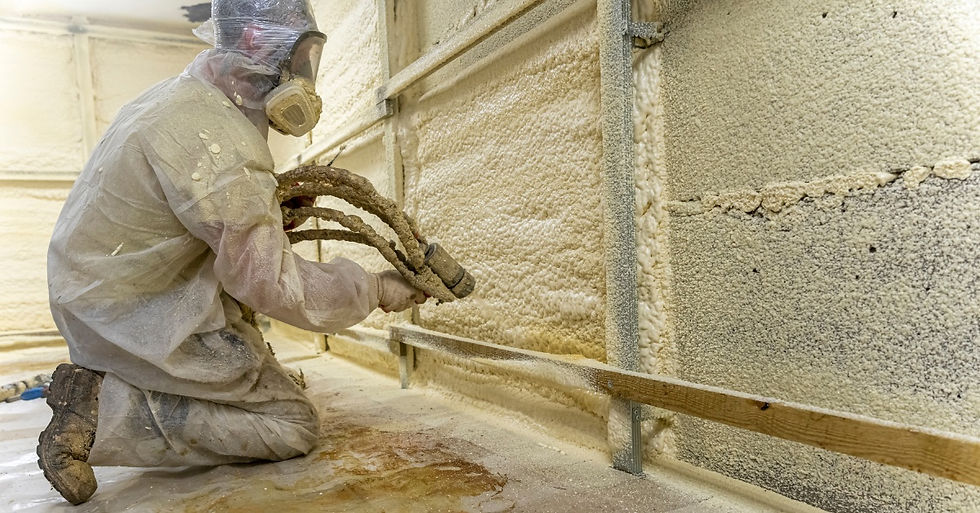 A person wearing a protective bodysuit kneels down with a spray hose while applying insulation into a wall.