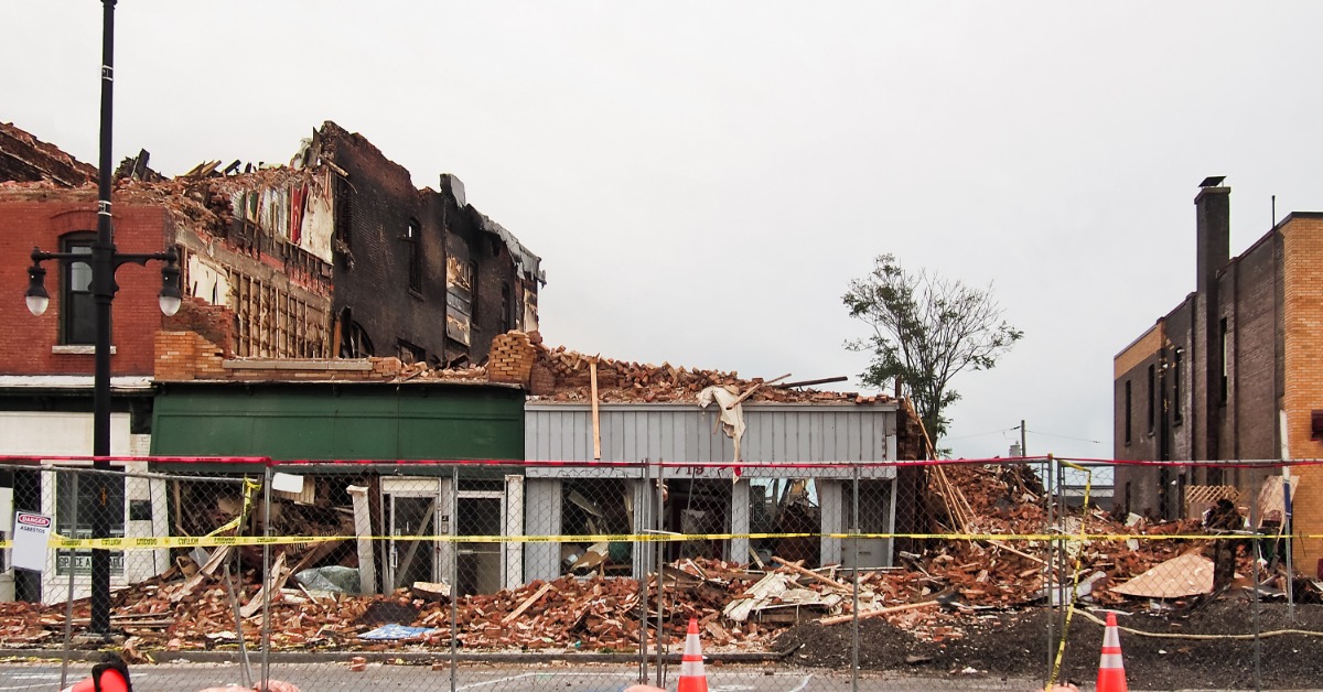 A storefront has suffered major damage and is in a sever state of disrepair. There is a fence blocking off the building.