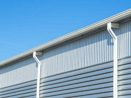 A commercial metal building with white gutters and downspouts along the roof edge under a clear blue sky.
