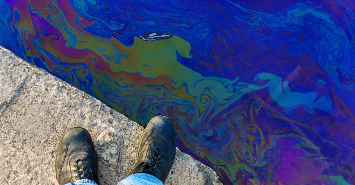 A person in blue jeans and black boot is standing on a ledge. Beyond the ledge is a chemical substance.