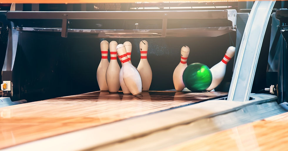 A green bowling ball knocking into white pins at the end of a lane. The pins have red stripes around the neck.