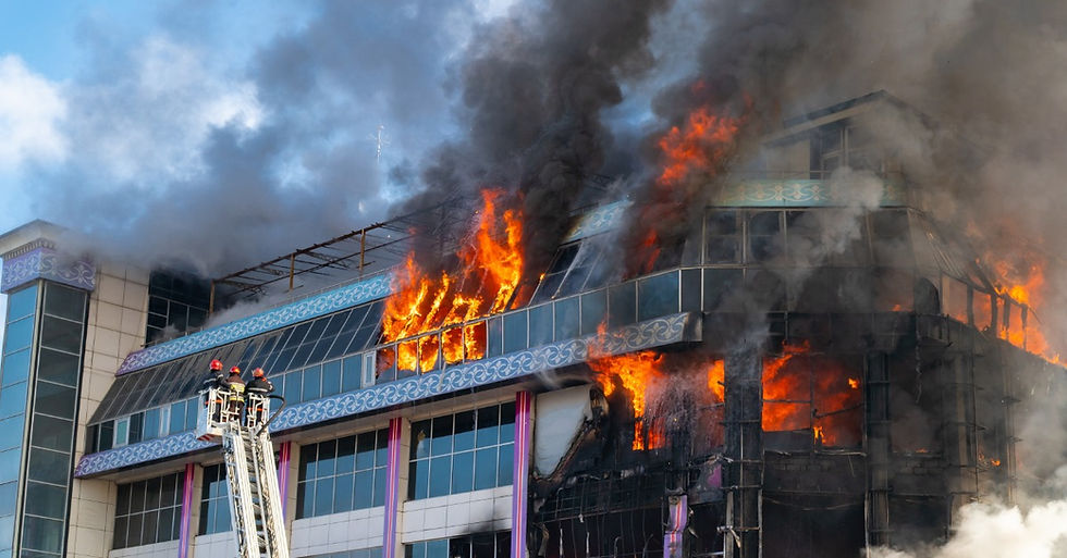 A building is on fire and there is a cherry picker with three firefighters in it. Smoke is billowing from the building.