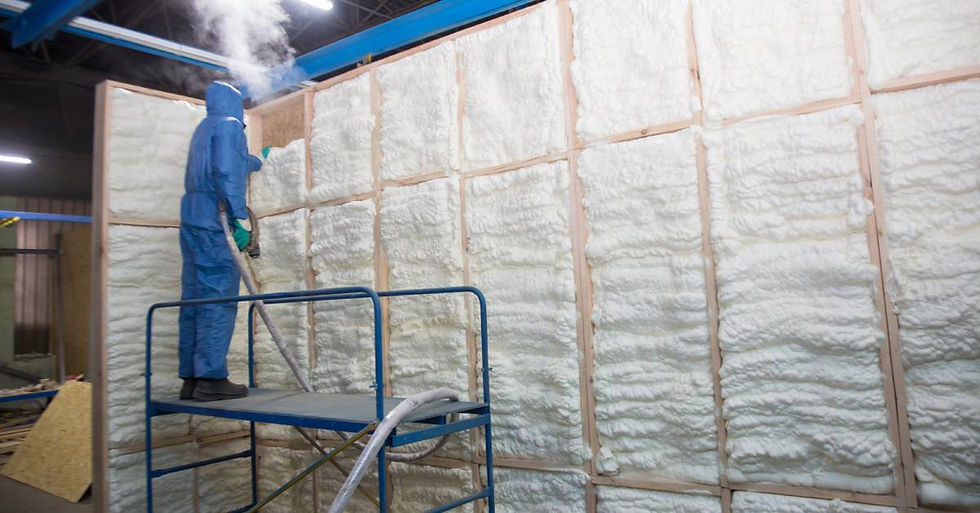 A worker wearing a blue protective body suit standing on scaffolding while using a gun to apply spray foam insulation to a wall.