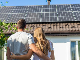 A young couple holding each other while looking at the roof of their home. They have solar panels attached to the roof.