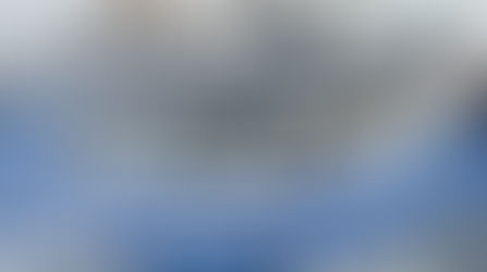 A large, metal industrial conveyor belt with a blue belt sits empty in an industrial space. The conveyor belt isn't moving.