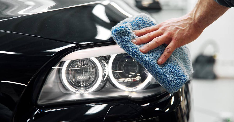 Someone wiping the headlight of a black car with a microfiber towel. The car's exterior is shiny under the room's lights.