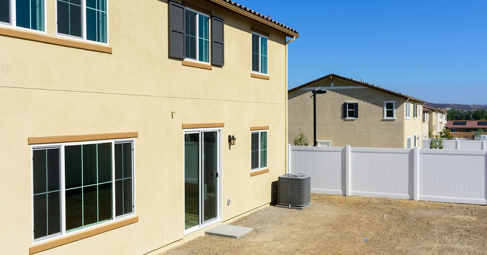 The back of a two-story house with an unfinished backyard. The house has multiple windows and a sliding door.