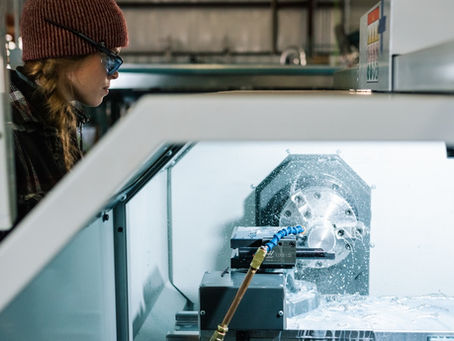 Operator observes CNC milling process inside machine, coolant spraying over rotating metal workpiece in workshop.